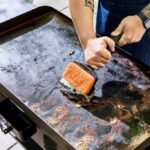 Person applying oil to a Blackstone griddle during the seasoning process