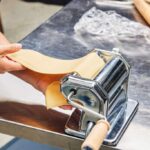 Shiny chrome steel pasta maker rolling perfect golden dough sheets on marble counter
