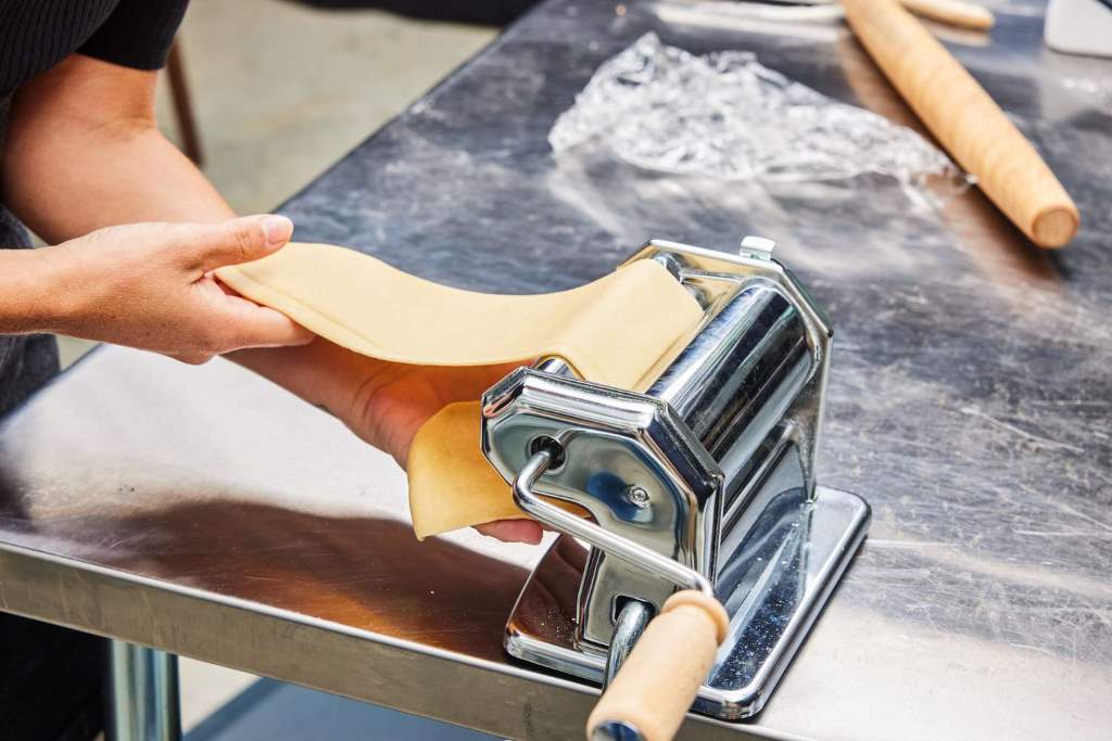Shiny chrome steel pasta maker rolling perfect golden dough sheets on marble counter