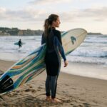 Surfer wearing a wetsuit and leash standing on the beach with a surfboard before entering the ocean