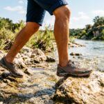 Person wearing affordable water shoes walking along a rocky Texas riverbank.