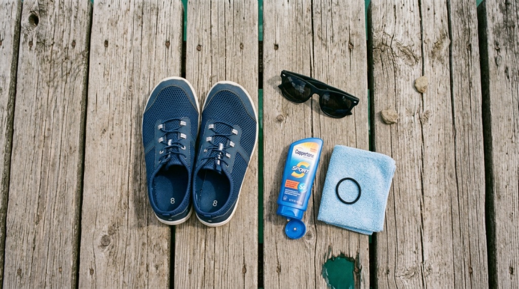 Budget water shoes, sunglasses, and sunscreen arranged near a Texas lake.