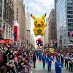 Crowds lining the street to watch giant balloons float past tall buildings during the 2026 Thanksgiving Day Parade