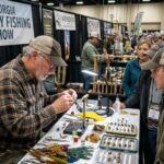 Fly tier building a trout fly at a demo bench during the Georgia fly fishing show