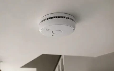 A white smoke alarm fixed to a hallway ceiling, a key part of home fire safety